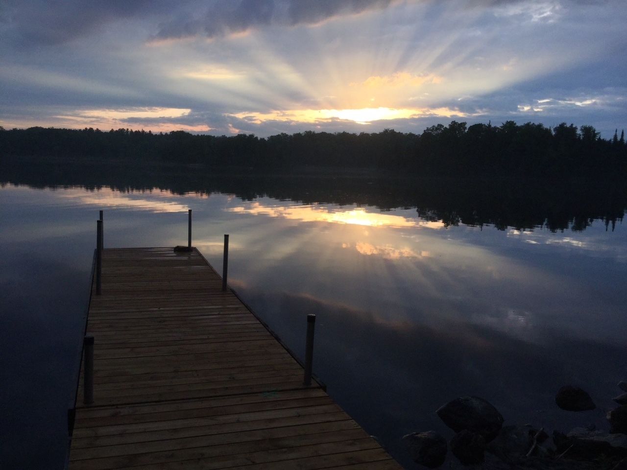 The sun is setting over a lake with a dock in the foreground