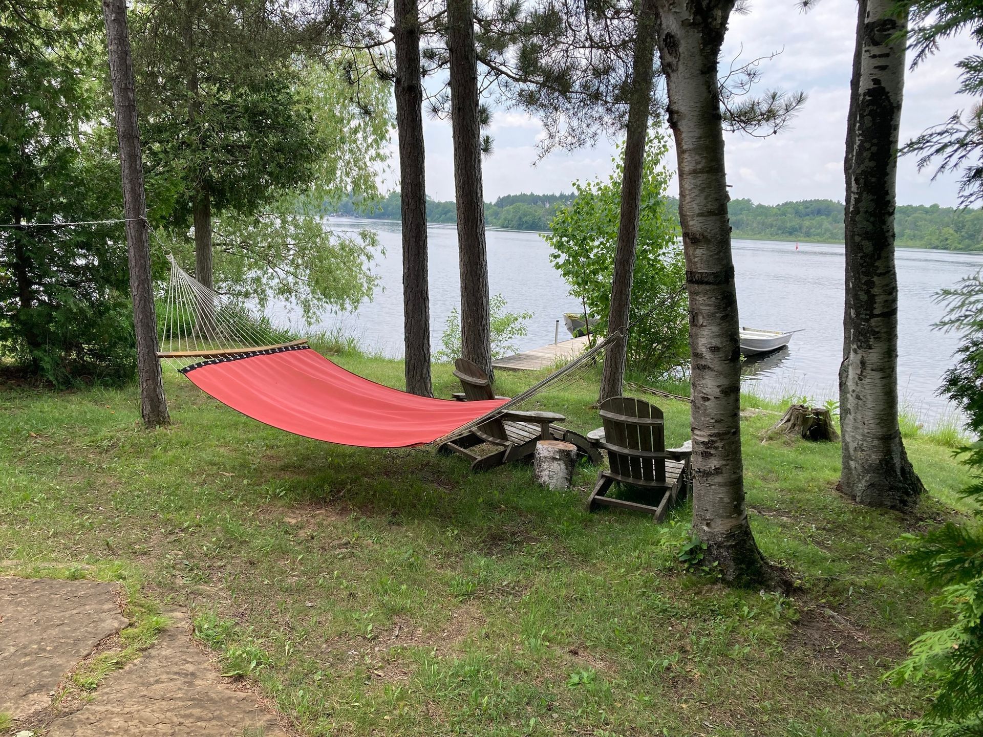 A red hammock is sitting in the middle of a lush green field next to a lake.