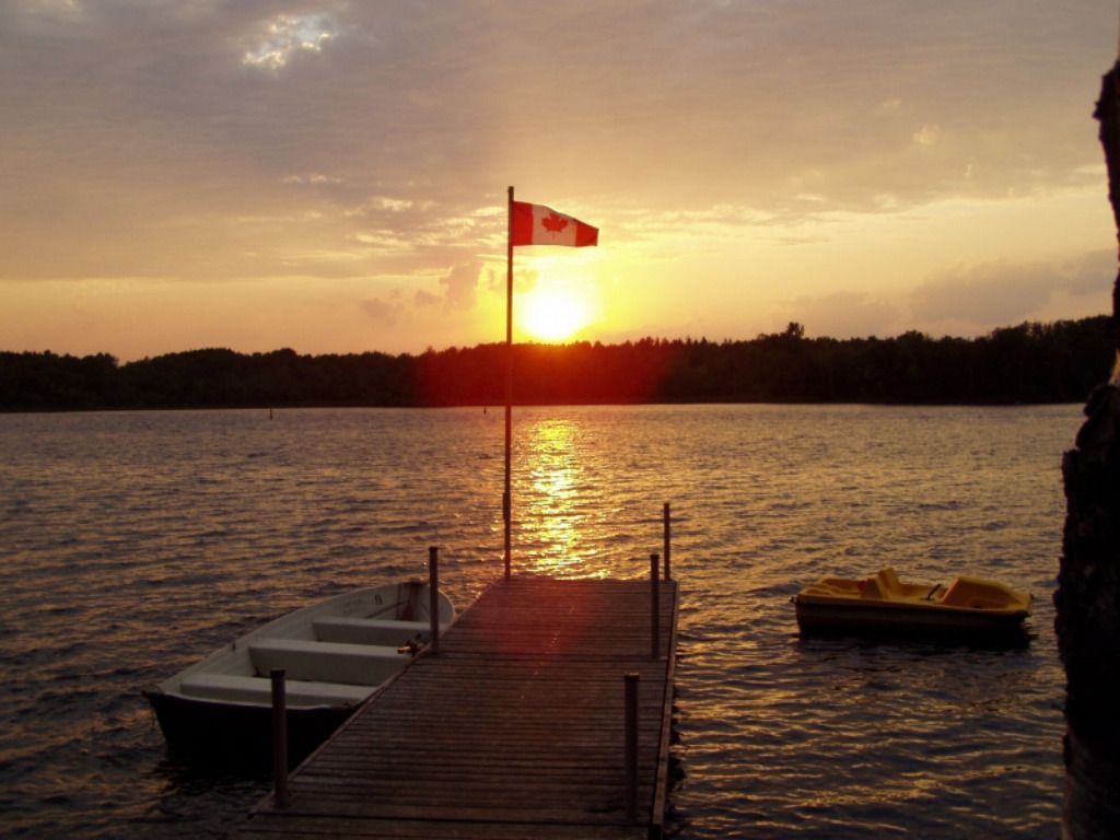 A sunset over a lake with a canadian flag in the foreground