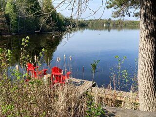 Two red chairs are sitting on a dock next to a lake.