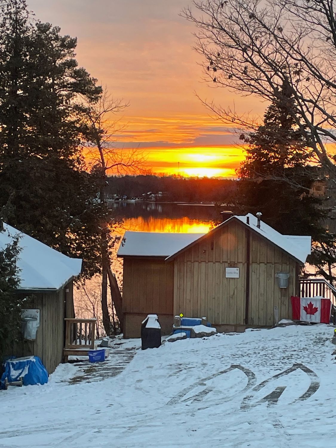A sunset over a lake with a canadian flag in the foreground