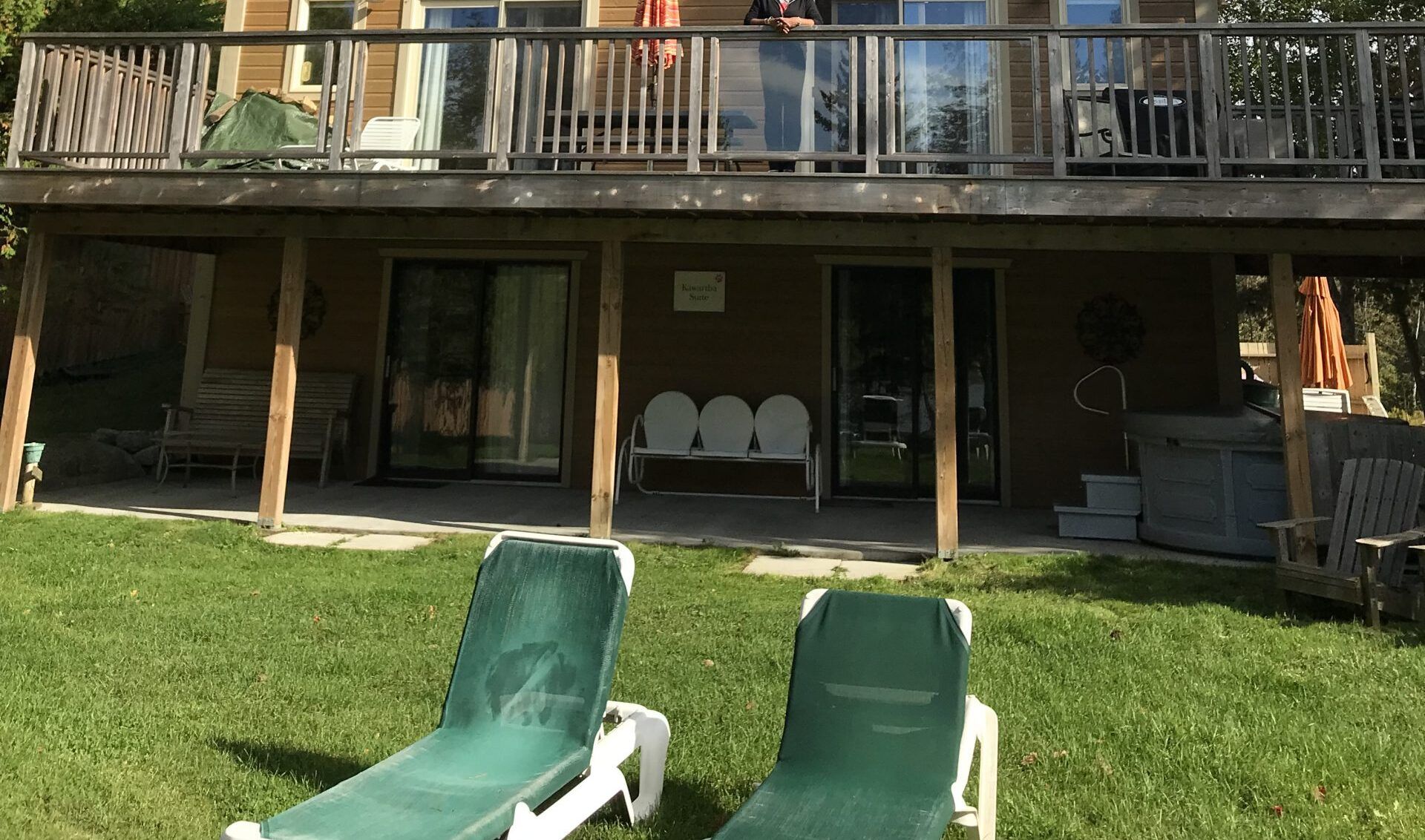 Two green lounge chairs are sitting in front of a house with a large deck.