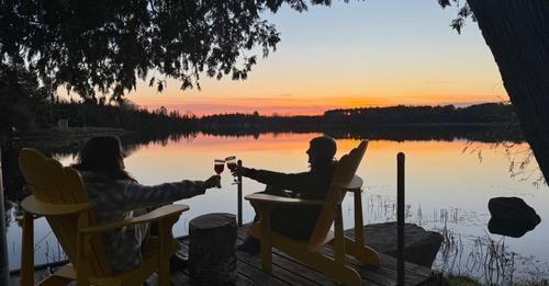 A man and a woman are sitting in chairs on a dock overlooking a lake at sunset.