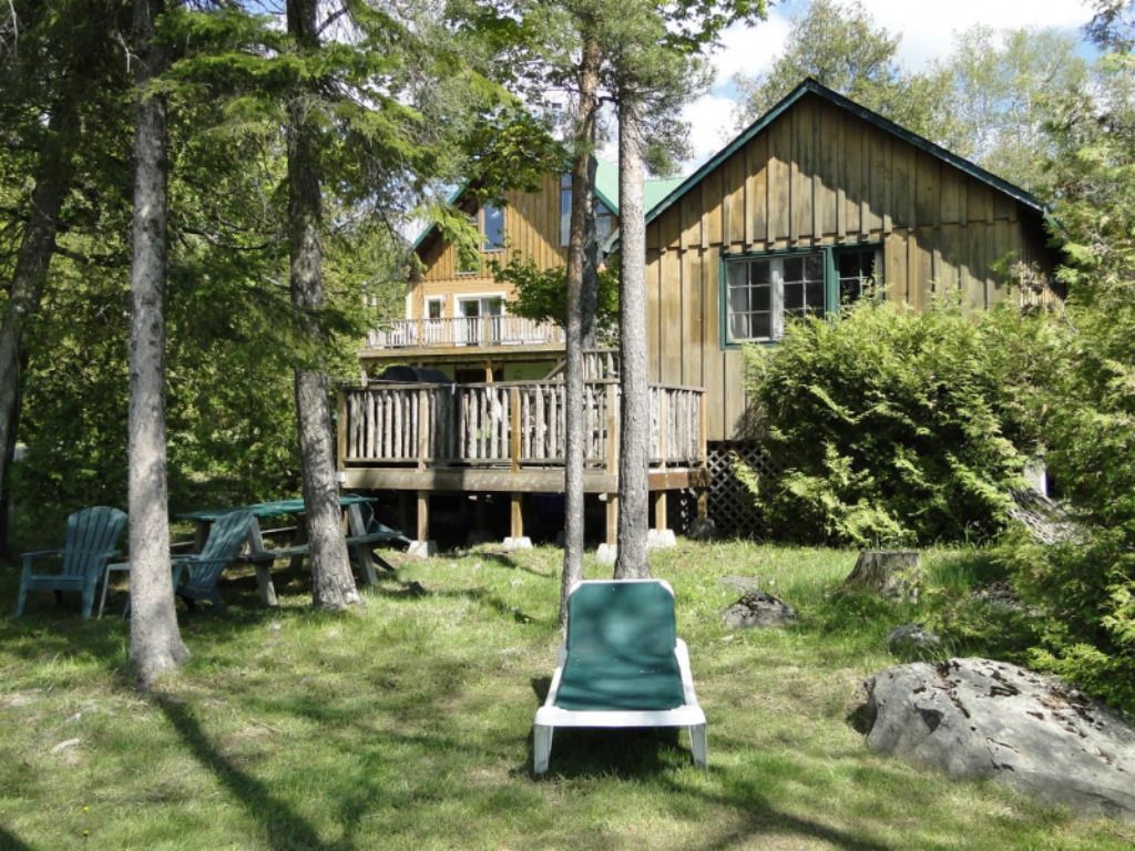 A large wooden house is surrounded by trees and chairs