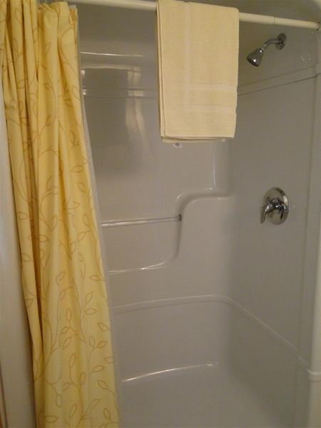A shower with a yellow shower curtain and two towels on the wall