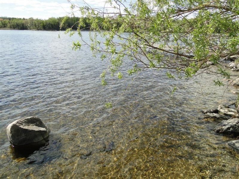 A large rock is sitting on the shore of a lake.