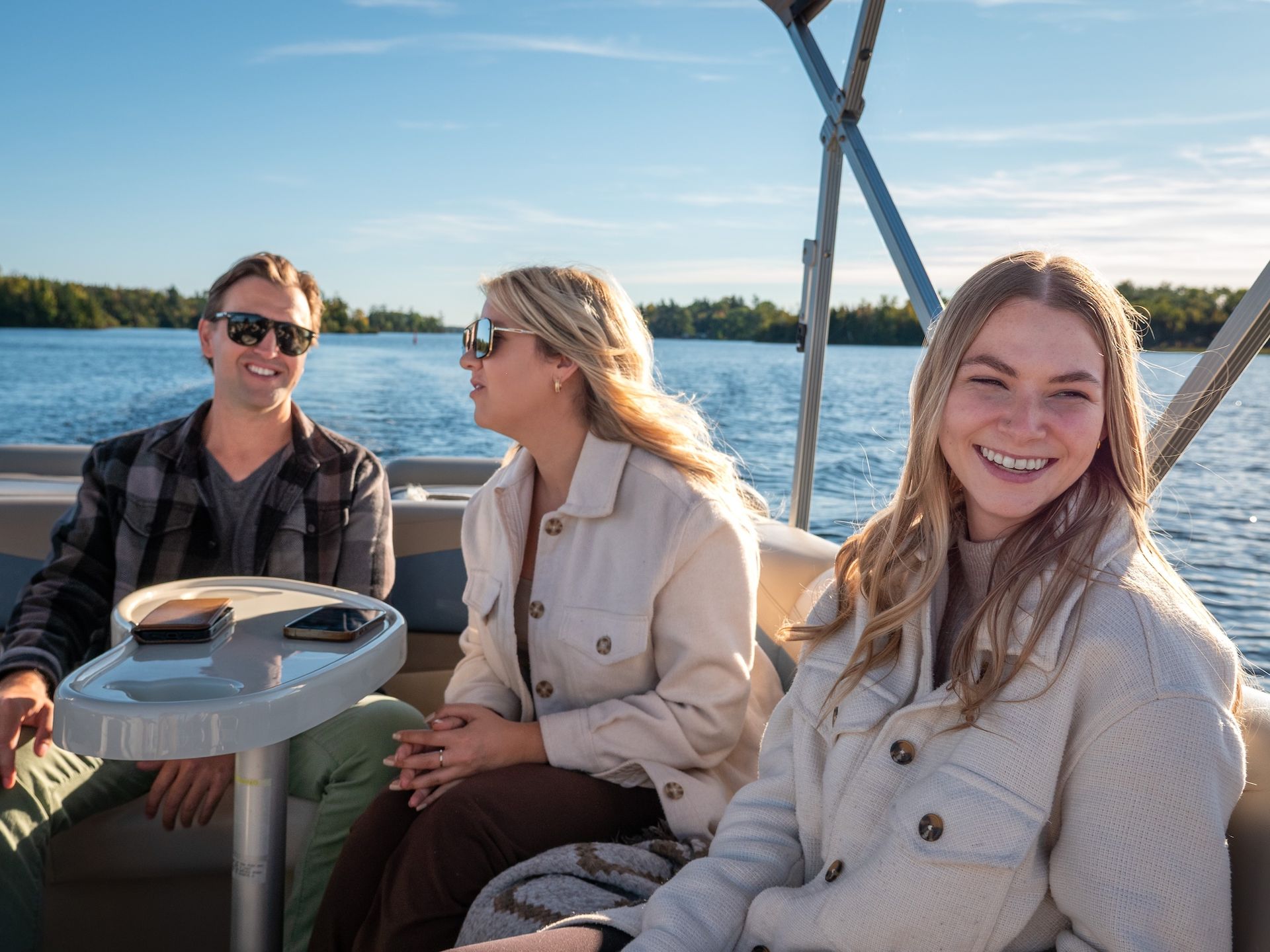 Three people smiling on a pontoon boat, enjoying a sunny day on the water.