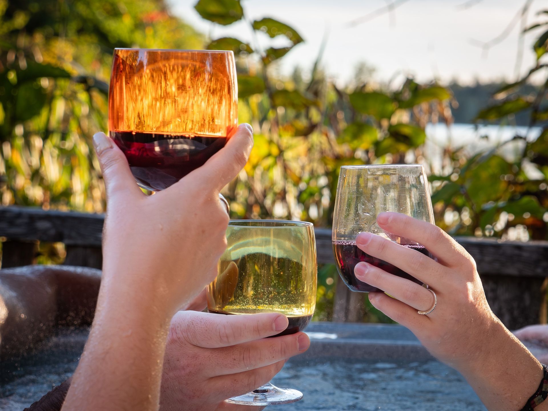 Three hands toasting with wine glasses in a hot tub, sun shining.