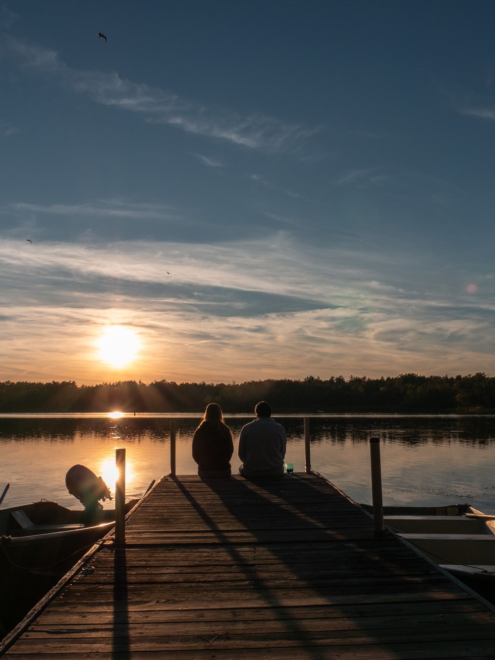 A man and a woman are sitting on a dock at sunset.