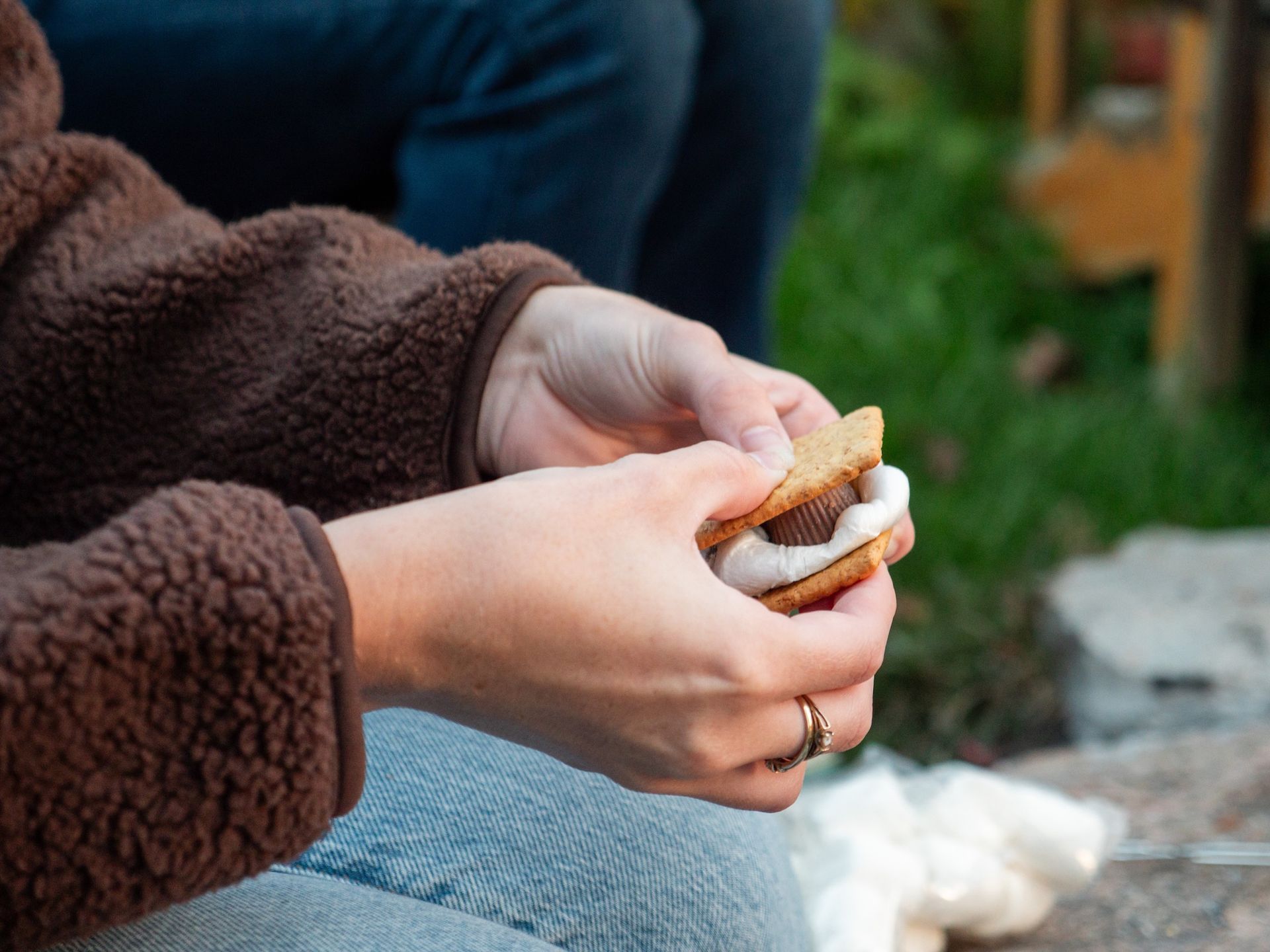 Person holding a s'more, with a melted marshmallow and chocolate between graham crackers.