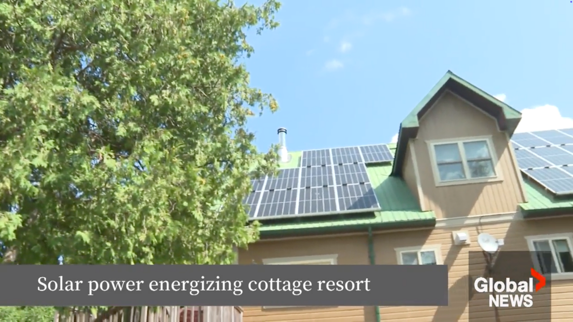 Solar panels on a green-roofed building, powering a cottage resort under a blue sky.