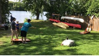 A group of people are playing a game of cornhole in a yard.