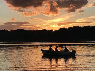 Two people are fishing in a boat on a lake at sunset.