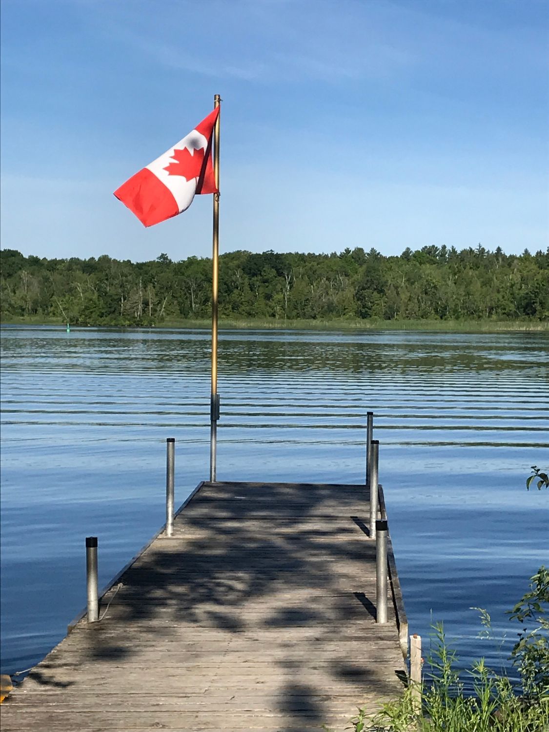 A canadian flag is flying on a dock overlooking a lake