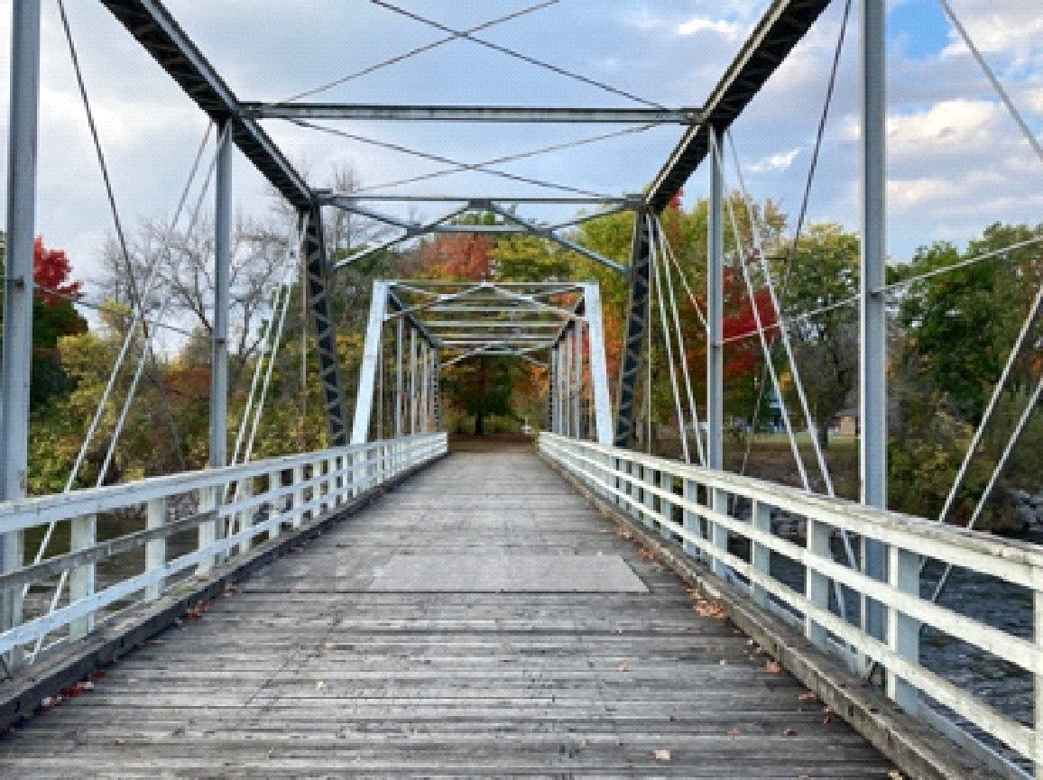 A wooden bridge over a river with trees in the background.