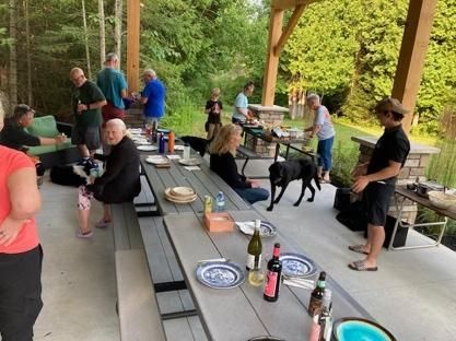 A group of people are gathered around a long picnic table.