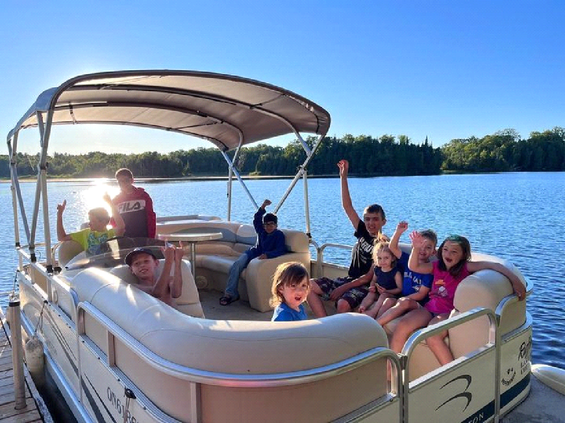 A group of children are sitting on a pontoon boat on a lake.