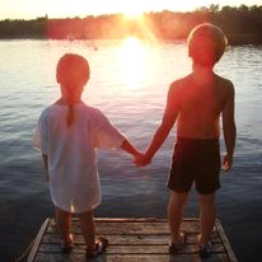 A boy and a girl are standing on a dock holding hands.