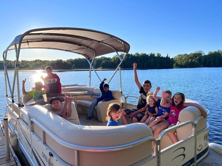 A group of children are sitting on a pontoon boat on a lake.
