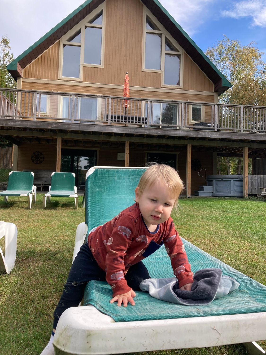 A baby is playing on a lounge chair in front of a house.