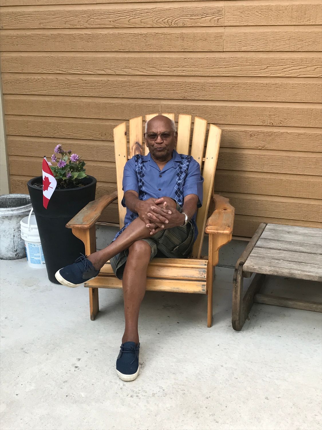 A man is sitting in a wooden chair on a patio.