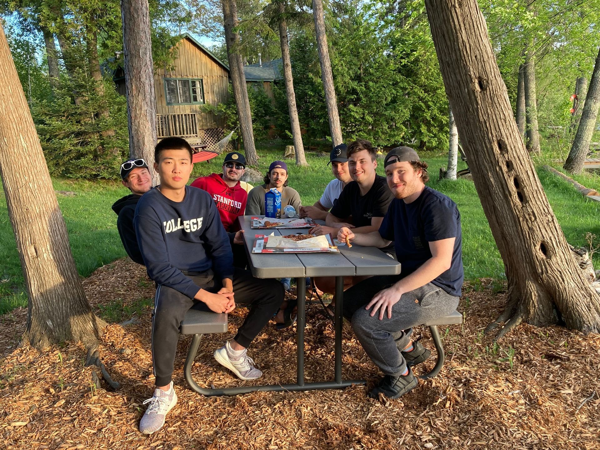 A group of young men are sitting at a picnic table in the woods.