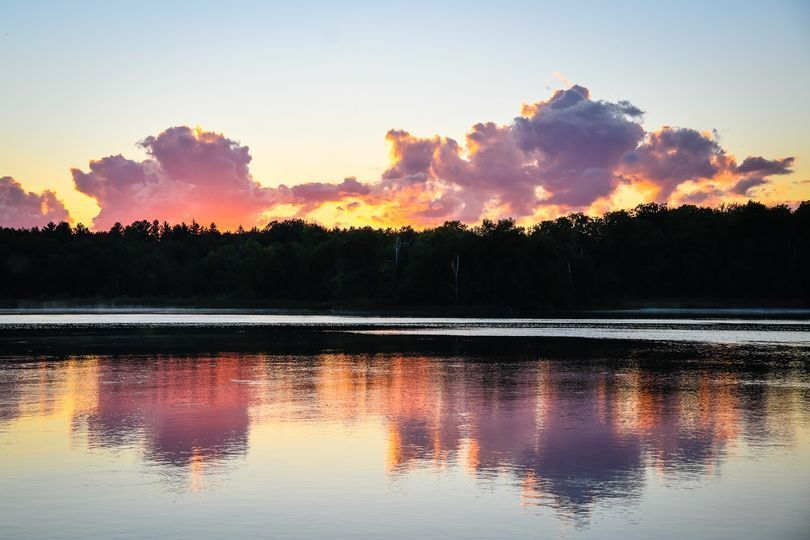 A lake with a sunset in the background and clouds reflected in the water.