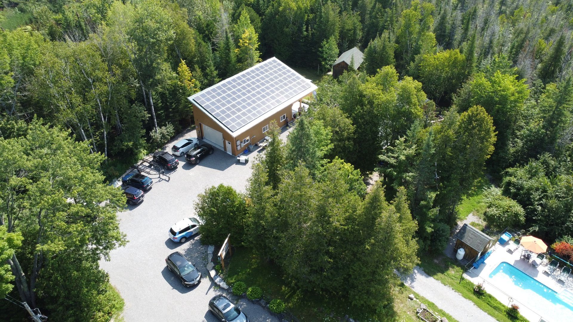 An aerial view of a house with solar panels on the roof surrounded by trees and a pool.