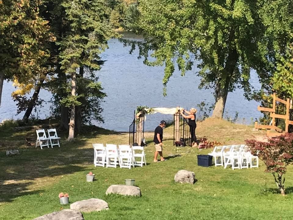 A group of people are standing in a grassy field in front of a lake.