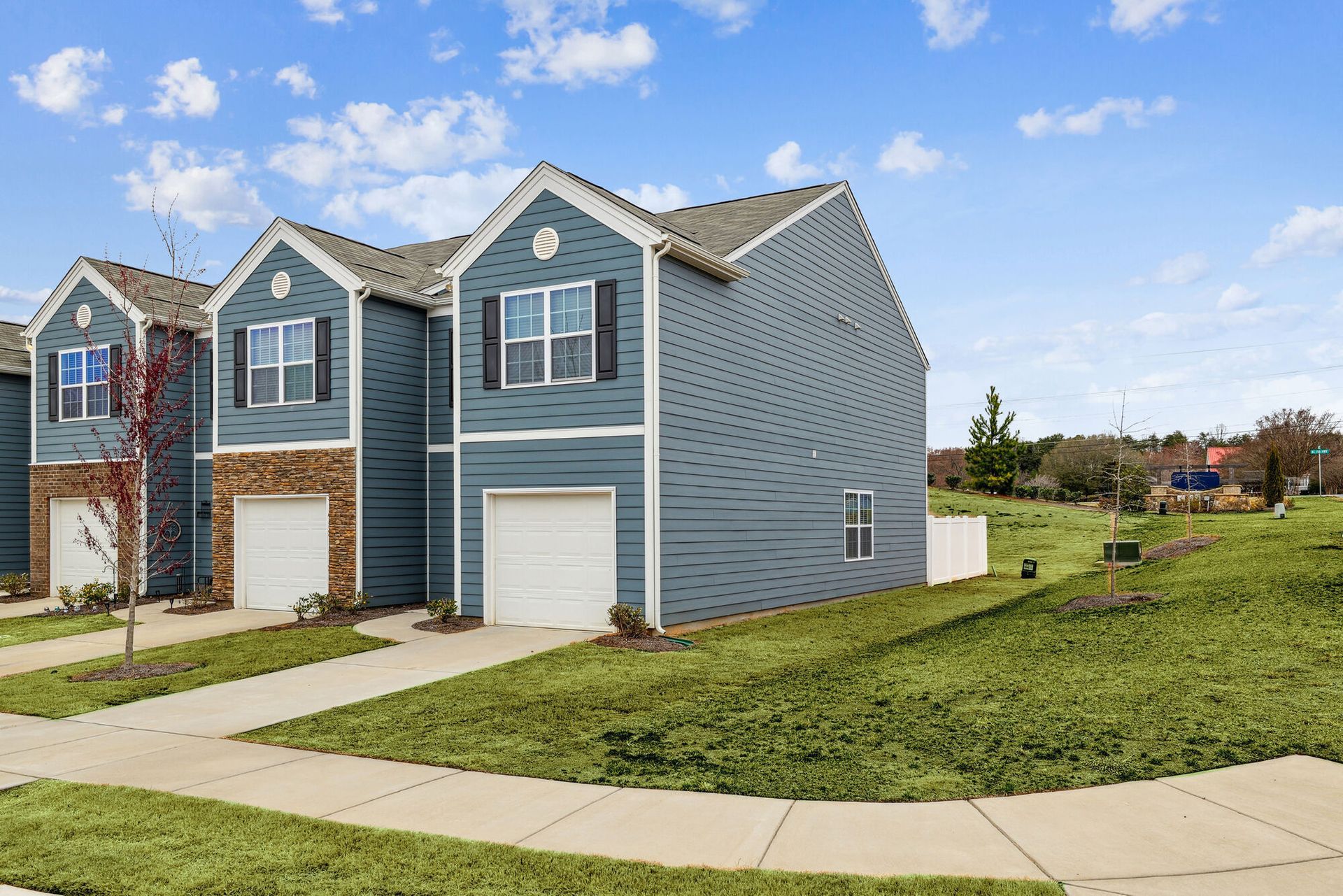 Townhouses with blue siding, white garages, and a grassy hill on a sunny day.