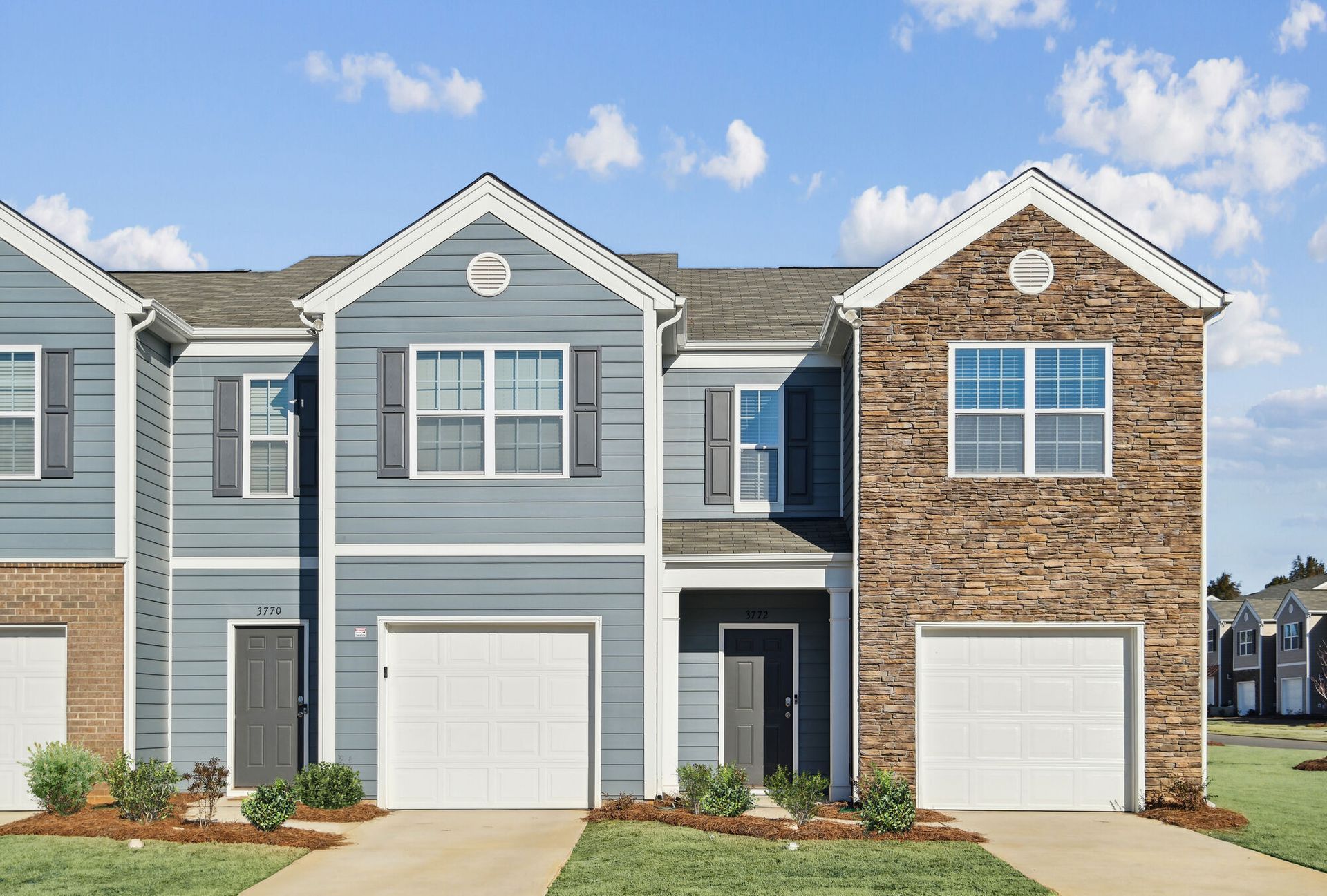 Townhomes with blue and stone exterior, white garage doors, and a blue sky.