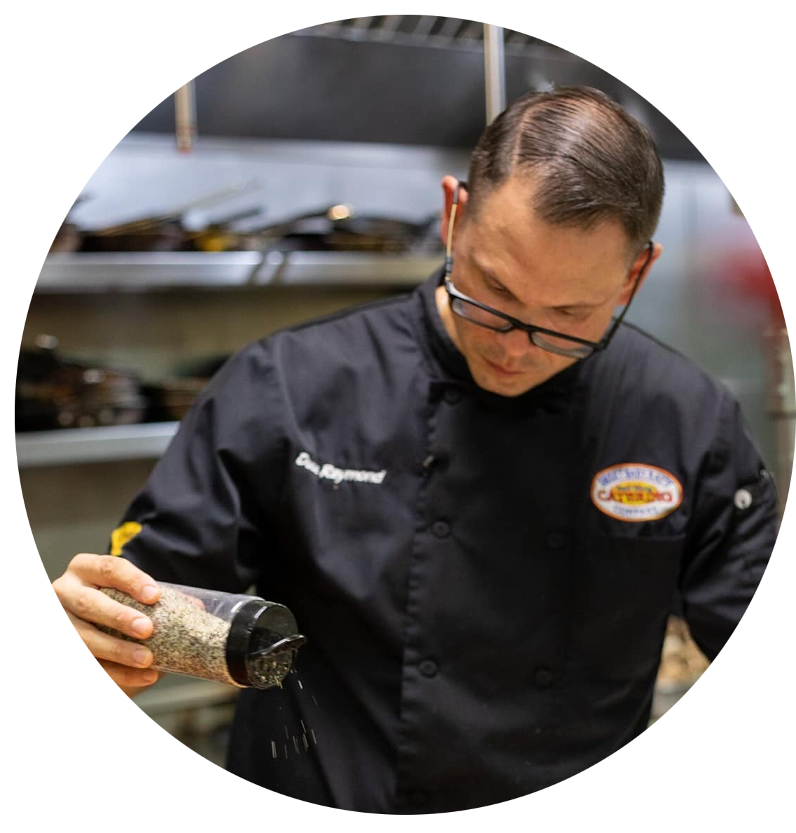 A man in a chef 's uniform is smiling in front of a brick wall