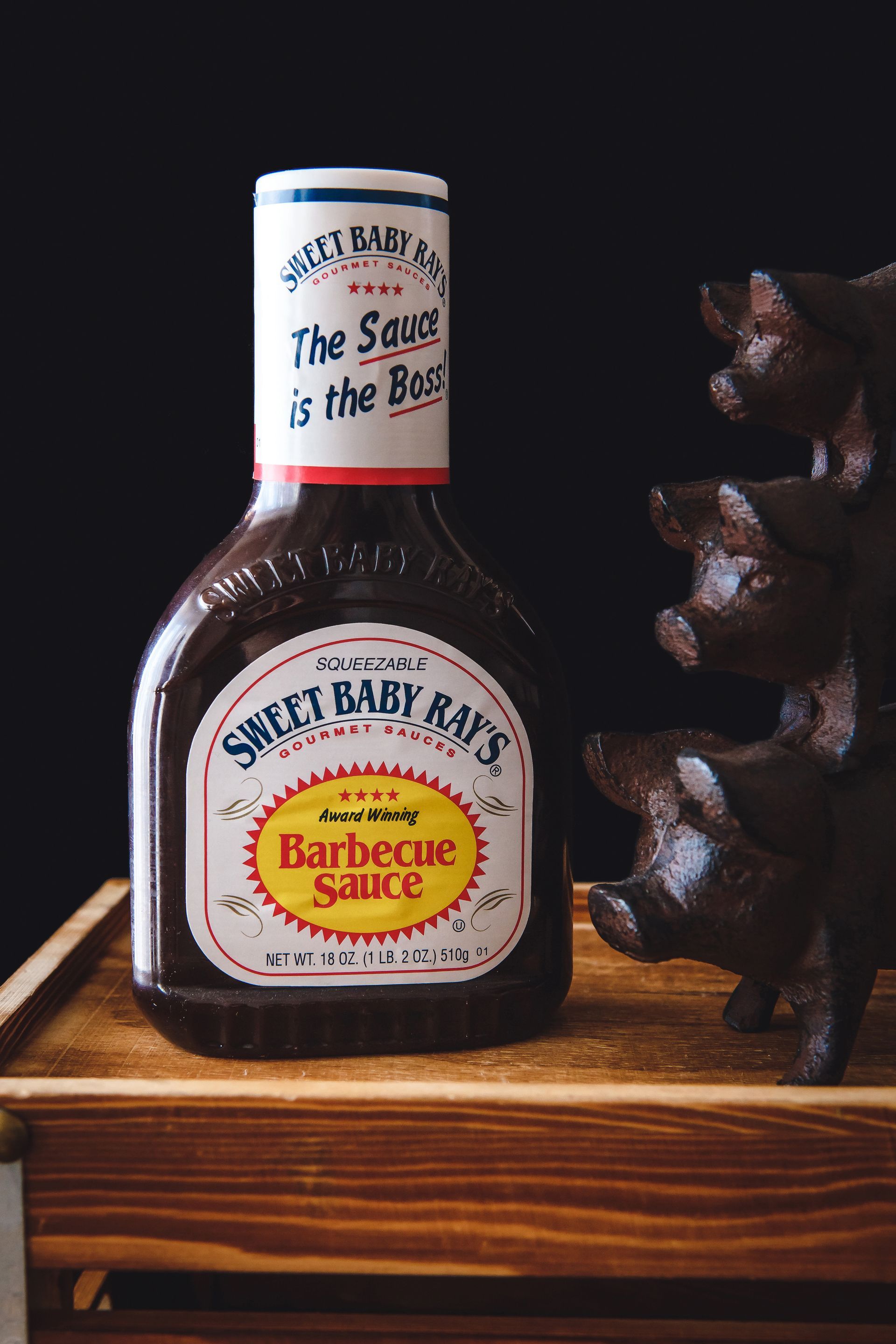 One bottles of barbecue sauce sitting on a wooden table next to a stack of pigs.