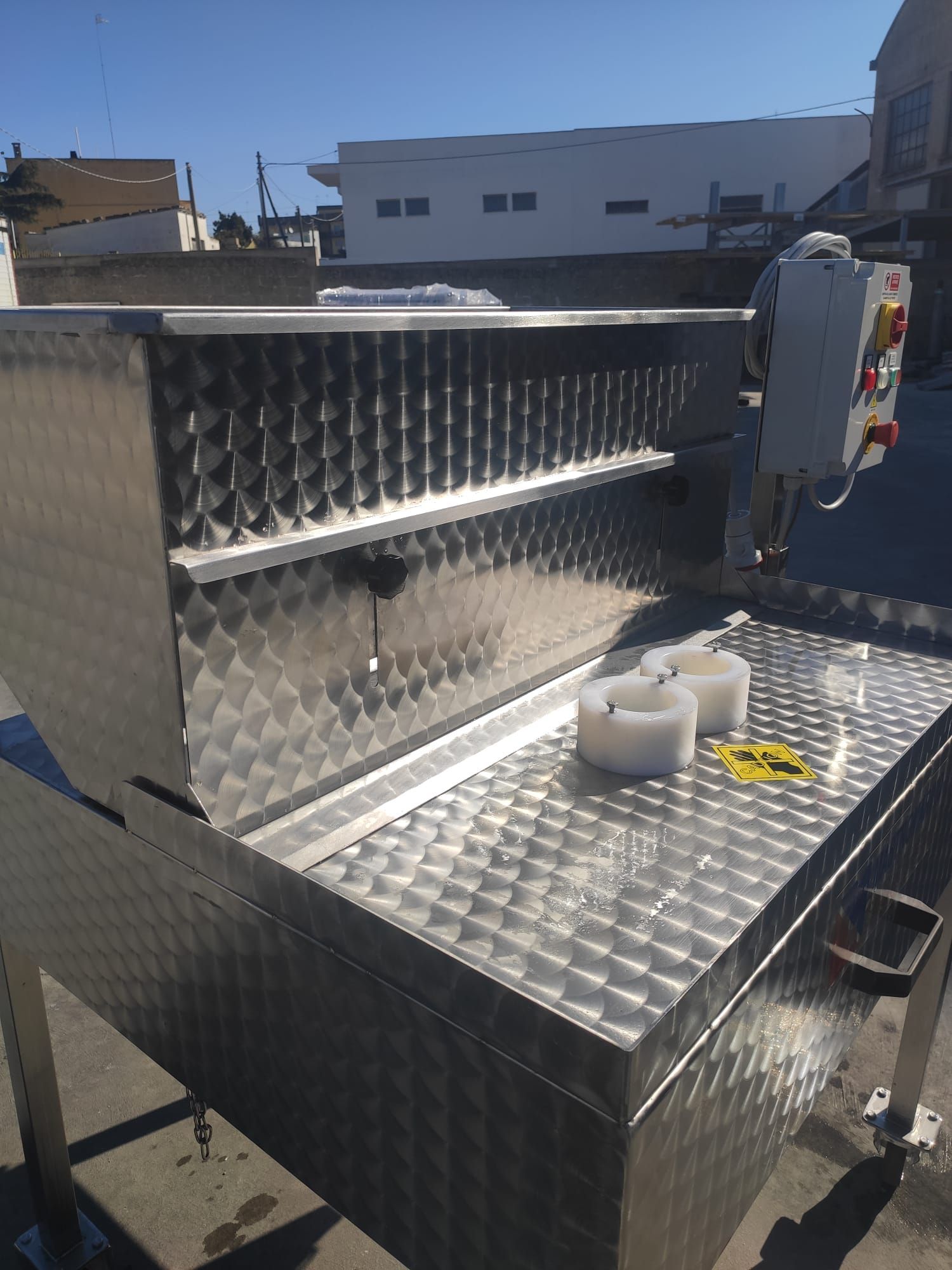 Macchina industriale in acciaio inox con scomparti angolari e pannello di controllo, all'aperto in una giornata di sole.