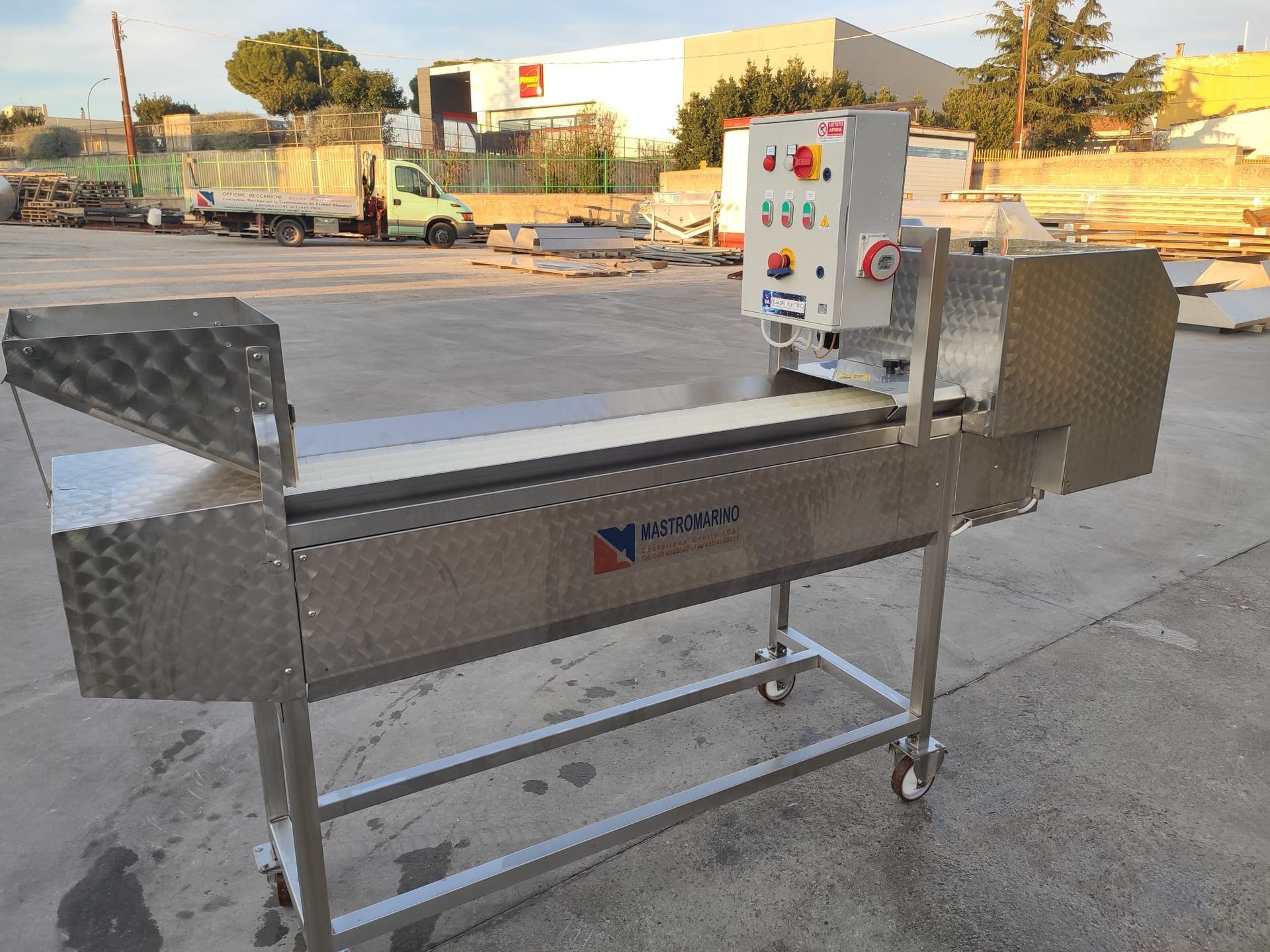 Macchina per la lavorazione degli alimenti in acciaio inox con nastro trasportatore, pannello di controllo, all'esterno.