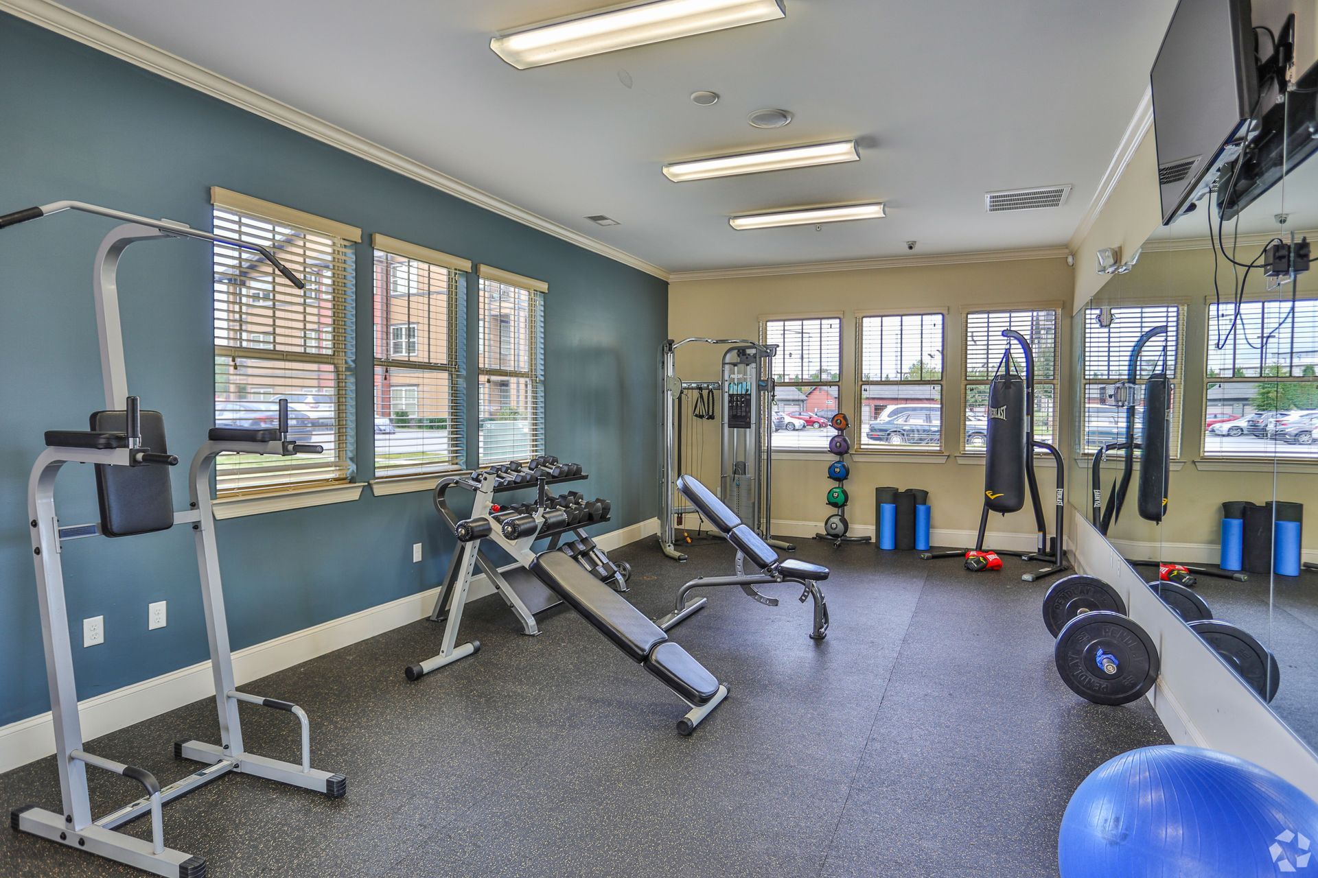A brightly lit, empty gym with exercise equipment including a weight bench, pull-up station, and a blue yoga ball at Riverwalk Apartments.