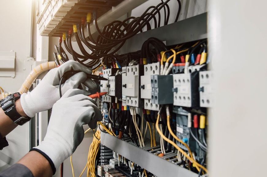 An electrician is working on an electrical box with a screwdriver.