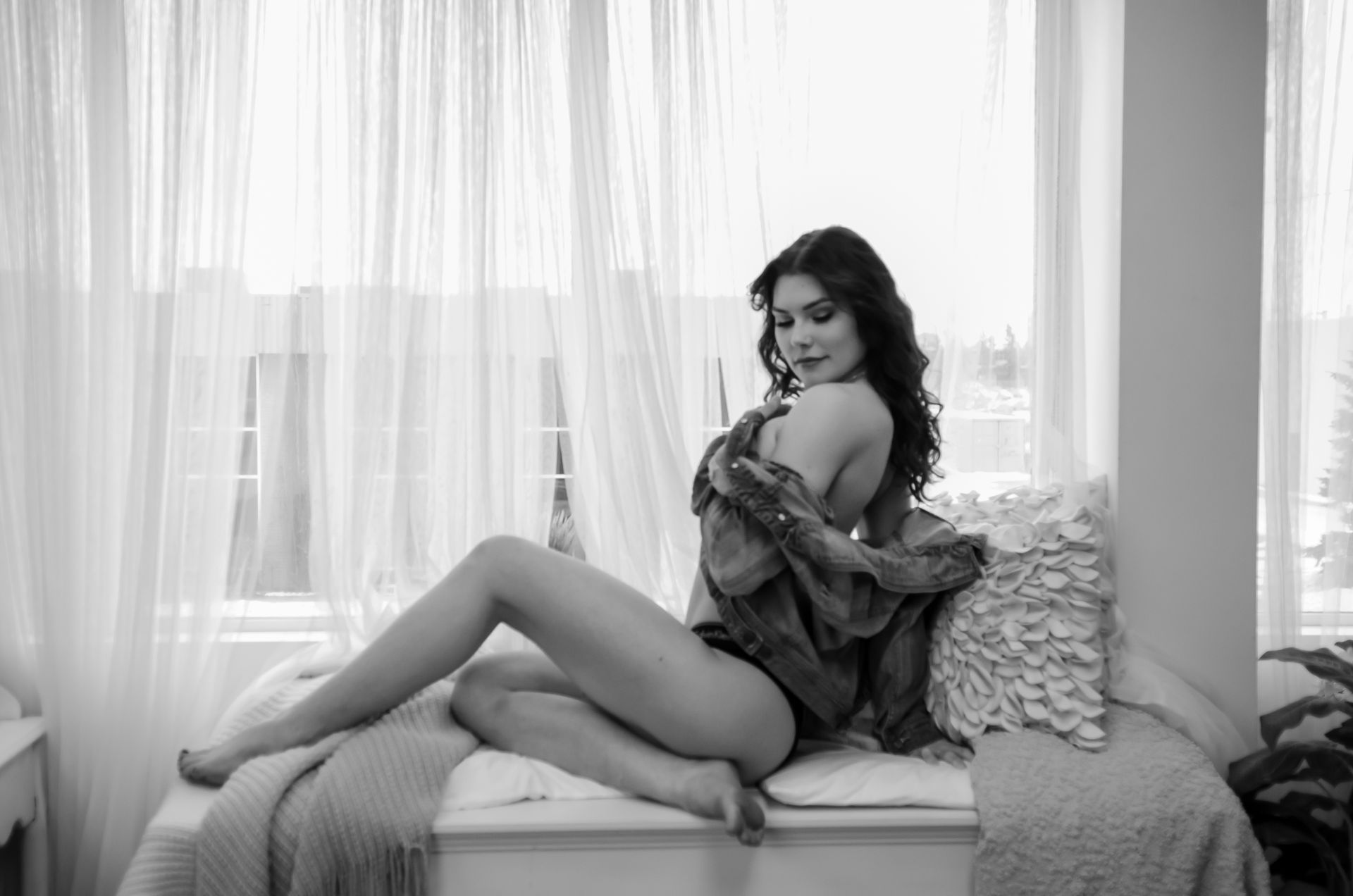Edmonton boudoir photo of woman in lingerie and denim jacket by window in black and white.