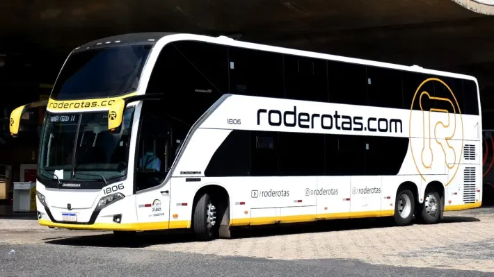 Um ônibus de dois andares com roderotas.com escrito na lateral está estacionado na beira da estrada.