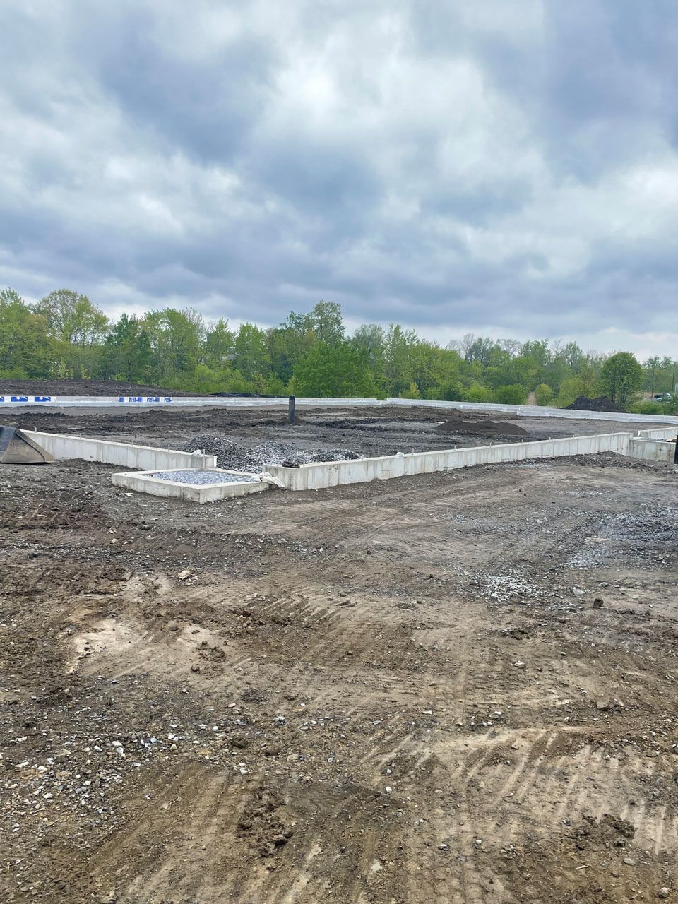 Gravel construction site with a concrete foundation under a cloudy sky