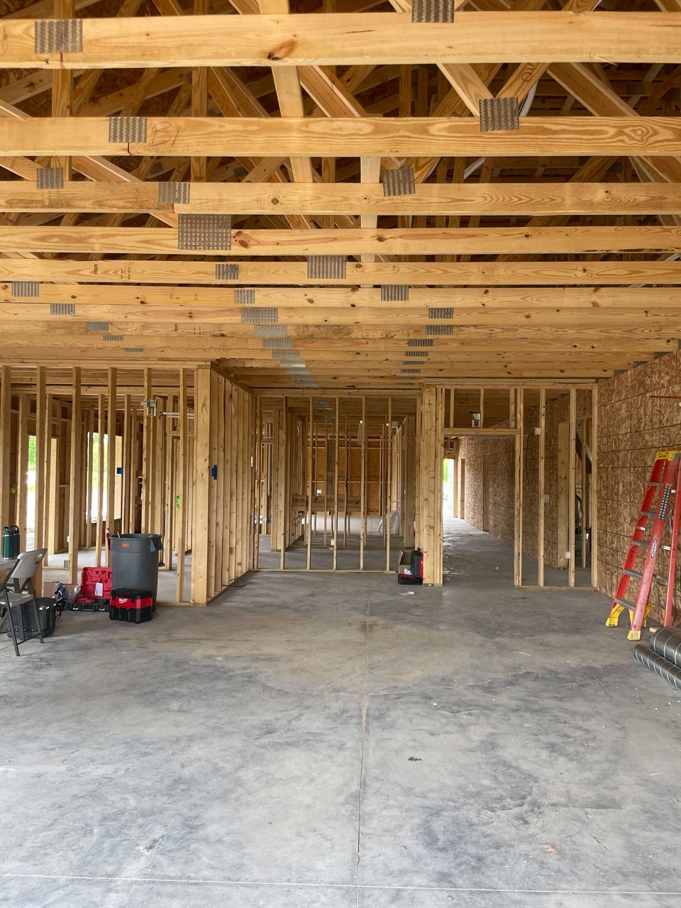 Interior of a framed house under construction with exposed wooden beams, concrete floor, and tools on the right