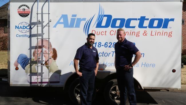 Two men standing in front of an air doctor duct cleaning and lining trailer