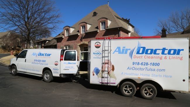 Two air doctor vans are parked in front of a house.