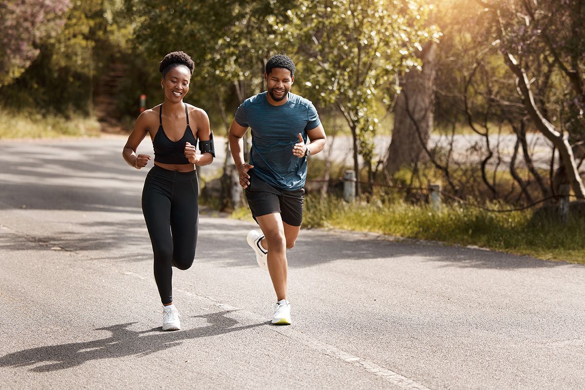 Two runners jogging on a sunlit road lined with trees