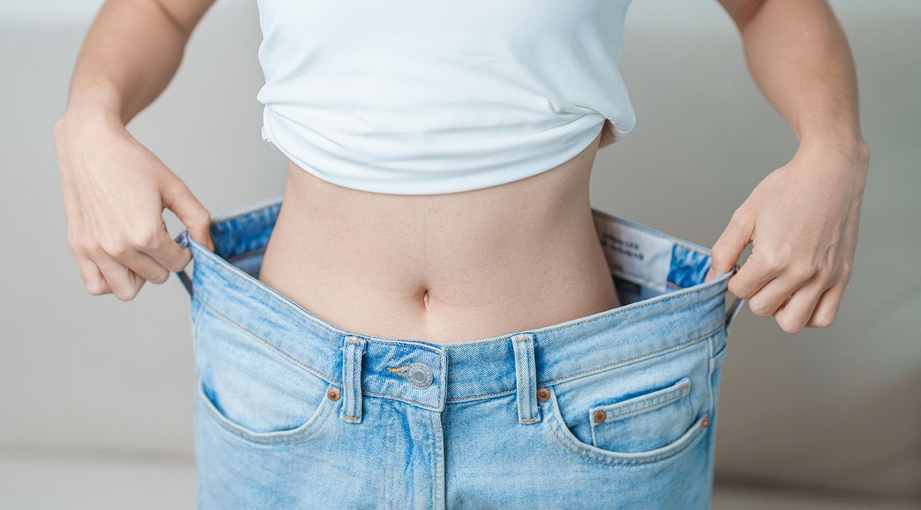 Person holding up oversized blue jeans around their waist to show weight loss