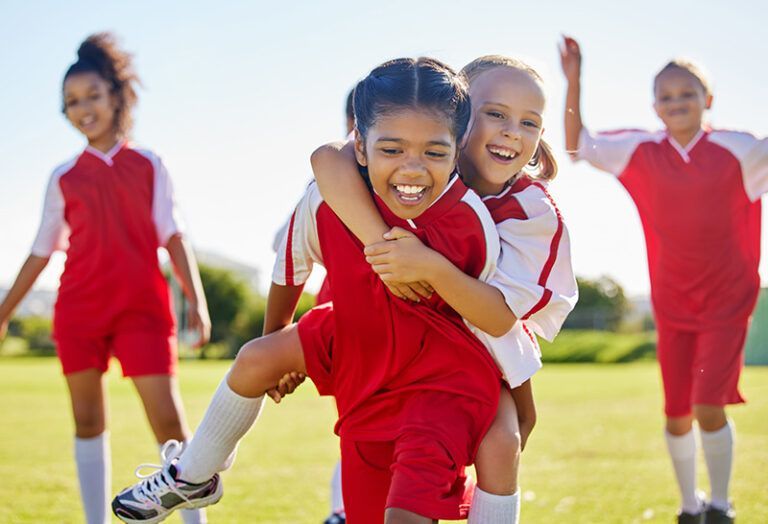 Children in red sports uniforms running and smiling on a sunny field