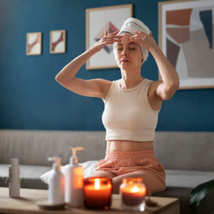 Person sitting on a couch applying a towel to their head, with candles and bottles on a coffee table in a blue living room.