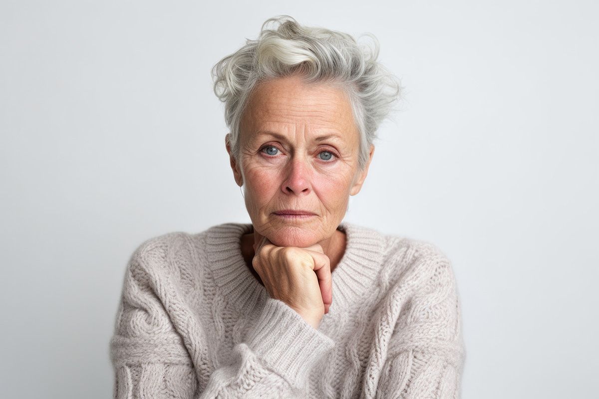 Thoughtful person with gray hair resting chin on hand against a light gray background