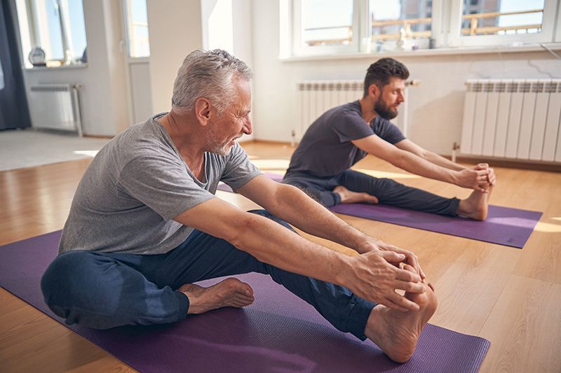 Two people stretching on yoga mats in a bright studio