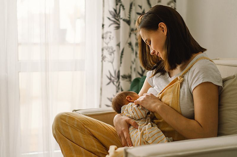 Woman breastfeeding a baby in a sunlit living room by the window